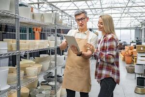 A customer consults with a shop assistant about flowerpots in a plant store, with the help of a tablet, in a bright commercial setting. photo