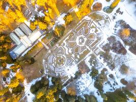 This aerial view captures the beauty of Konopiste rose garden in winter, featuring snow-covered paths and intricate garden layouts surrounded by frosted trees. photo