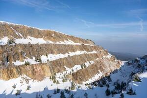 Snow blankets the rugged terrain of the Stanislaw Quartz Mine, showcasing the geological strata under a bright winter sky. The Izera Mountains provide a beautiful backdrop. photo