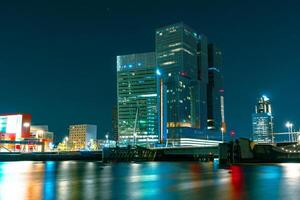 A stunning nocturnal view of Rotterdam's high-rise architecture standing tall against the backdrop of the starry night sky, creating a magnificent and captivating urban scenery. photo