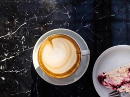 A cup of coffee sits on a table next to a slice of cake photo