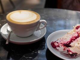Cup of coffee sits on a saucer next to a slice of cake photo