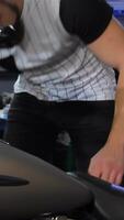 Focused man squats beside a sleek chopper in a bustling motorcycle workshop video