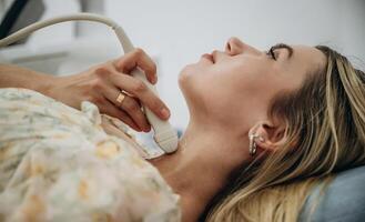 Woman is lying down, and undergoing ultrasonic test of the thyroid gland photo