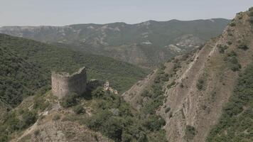 Ancient close up stone fortress ruin on mountain ridge surrounded by forested valleys and distant peaks in summer daylight, aerial view. video