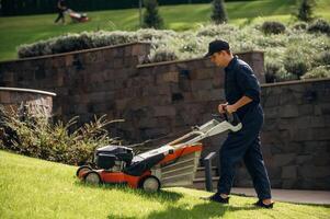 View from ,the side, cutting grass by lawn mover. Professional gardener is on the lawn photo