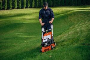 Process, of cutting the, grass by using lawn mover. Professional gardener is on the lawn photo