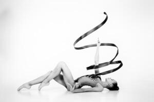 girl from rhythmic gymnastics in a bodysuit shows an exercise with a ribbon lying on her back photo