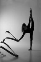 a girl from rhythmic gymnastics in a standing bodysuit shows an exercise with a ribbon in vertical splits. photo