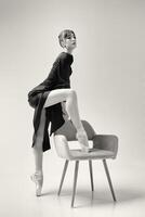 a ballerina in a black dress stands showing a deflection and plasticity and putting her foot on a chair. photo