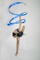 a girl from rhythmic gymnastics in a bodysuit rotates a ribbon, while sitting on a cube photo