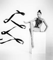 girl from rhythmic gymnastics, in a bodysuit rotates a ribbon while sitting on a cube photo