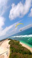 Cinematic FPV drone shot of paragliders gliding over cliffs and turquoise ocean at Pandawa Beach, Bali. Aerial view of scenic coastline, tropical waves, and summer sky. video