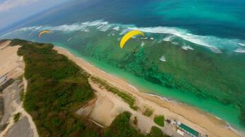 Cinematic FPV drone shot of paragliders gliding over cliffs and turquoise ocean at Pandawa Beach, Bali. Aerial view of scenic coastline, tropical waves, and summer sky. video