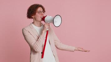 Caucasian young man with curly hair talking with megaphone, proclaiming news, loudly announcing advertisement discounts sale, using loudspeaker to shout speech. Happy guy isolated on pink background video