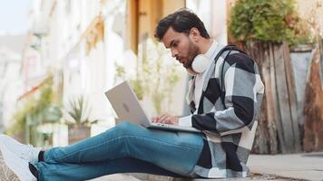 Displeased Indian man using laptop typing browsing working, loses becoming surprised sudden lottery results bad news fortune loss game fail computer virus. Arabian guy sitting on urban city street. video