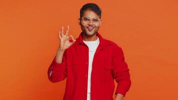 Okay. Happy Indian man looking approvingly at camera showing ok gesture, like sign positive feedback, approve something good celebrate victory wink blink eye flirting. Arabian guy on orange background video
