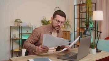Stressed young businessman looking at unpaid bank debt bills, doing paperwork, planning budget calculate finances mortgage payments. Freelancer guy throws paper bills sitting at home office table desk video