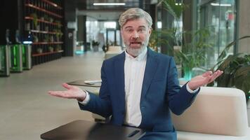 What. Why. Angry Caucasian businessman raising hands in indignant expression, asking reason of failure, demonstrating disbelief irritation by troubles. Bearded guy in suit sitting in office lobby. video
