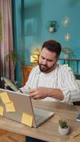 Tired exhausted fatigue business man office employee manager sits in home office table, with laptop sticky notes with many tasks inscription help feels sad boredom overworked multitasking. Vertical video