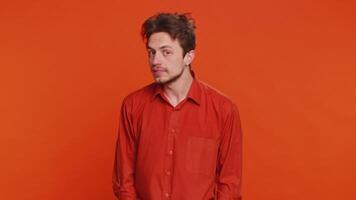 Knock-knock who is there. Confused excited Caucasian man knocking door gesture asking who is at home feeling embarrassed, no idea, being clueless and uncertain. Young guy isolated on orange background video