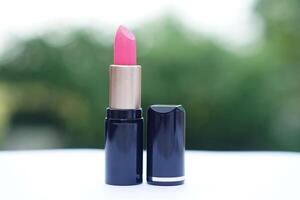 A single pink lipstick in a sleek black and gold tube, placed on a white surface with a soft green background. Concept, beauty , cosmetic, skincare branding, or product showcases. photo