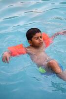 A young boy floating in a pool with his arms outstretched photo