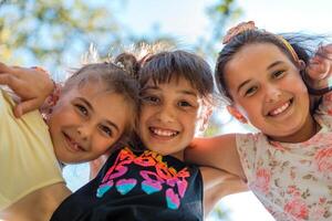 Happy children embracing each other having fun and smiling at the camera with a sky background, a group of joyful kids playing together outside. photo