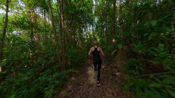 Dynamic FPV drone shot of woman running through lush tropical jungle path, capturing fitness, freedom, and nature in motion. Ideal for wellness, travel, and adventure themes. video