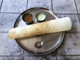 Indian masala dosa served with sambhar and chutney on a round metal plate. photo