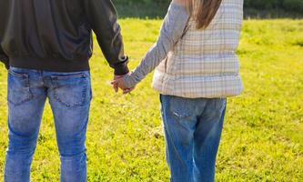 Close-up of couple in love walking in the autumn park holding hands looking in the sunset. photo