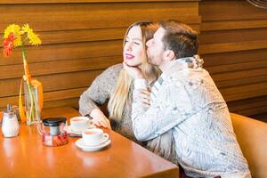 Young man kissing her girlfriend in the cheek while having some tea together in a cafe photo