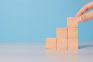 Man's hand organizing wooden blocks on blue surface. Symbolizes workflow, step-by-step strategy, or structure photo