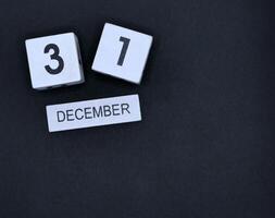 Wooden calendar, December 31st, New Year's Eve on black background photo
