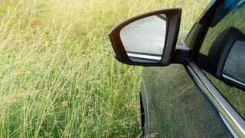 Abstract mirror view of the side of a navy blue car. Driving through the lush green grass. photo