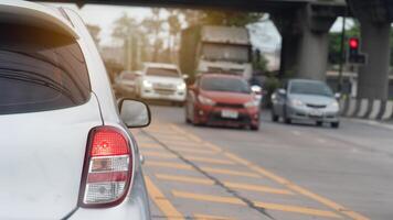 Black side of car with turn on brake light. Side of car with yellow line indicates the median strip area. Several cars from the opposite direction head towards an intersection with traffic lights. photo