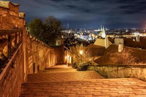 Under the moonlight, the Prague Castle staircase reveals a stunning view of the city's illuminated skyline. The warm light creates a captivating ambiance, inviting evening strolls. photo