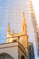 St Andrew Undershaft Church stands in striking contrast to the sleek, glass facade of a modern skyscraper in London. This scene captures the blend of history and contemporary architecture. photo