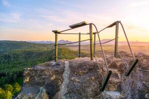 Enjoy a breathtaking sunset over the Lusatian Mountains from the rocky vantage point of Popov Cliffs. The warm evening light casts a golden hue across the sandstone formations and lush forests. photo