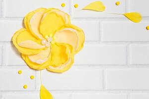 White Brick Background With Big Handmade Yellow Flower and Empty Place for Text photo