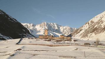 Aerial view Ancient Lamaria Monastery in snowy highland valley, surrounded by Caucasus peaks, part of UNESCO listed Upper Svaneti region video