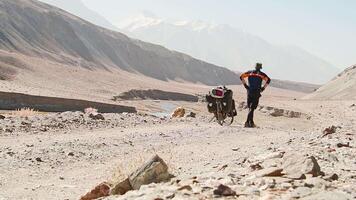 Static view adventurous fit traveller cycle bicycle touring solo in remote high Pamir mountains early morning by river. Pamir highway Bartang valley video
