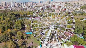 Yerevan, Armenia - 19th october, 2024- Aerial zoom out view ferris wheel in Victory Park ir with cityscape and buildings of Yerevan. Sunny autumn day carousels day out things to do concept video