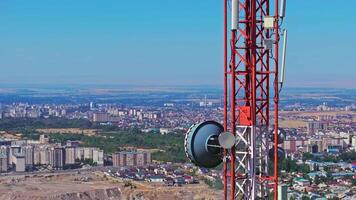 A stationary aerial close-up of a large microwave antenna mounted on a red and white telecommunication tower. The structure stands against the cityscape of Bishkek, showcasing urban infrastructure. video