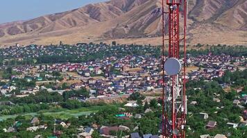 Drone footage showing a mountain village near with a telecom tower on a dry hill. The drone flying slowly in an arc around the tower, creating a parallax effect with distant foothill in the background. video