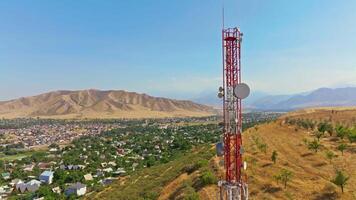 Drone footage showing a mountain village near with a telecom tower on a dry hill. The drone moving slowly in an arc around the tower, creating a parallax effect with distant mountains in the background. video