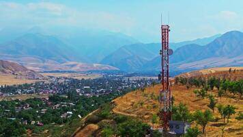 Drone footage showing a mountain village near with a telecom tower on a dry hill. The drone flying slowly in an arc around the tower, creating a parallax effect with distant mountains in the background. video