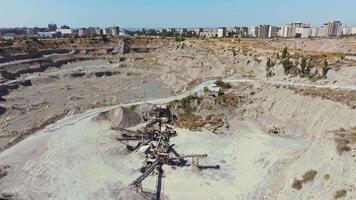 Aerial drone footage of a sand and gravel quarry in South Bishkek, showing crushers in operation. The drone moves down-forward, capturing the excavation site with sandy terrain and urban buildings in the background under a clear sky. video