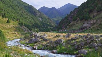 Handheld static view of a mountain valley with a winding stream, Corral, green hills, and scattered trees. Overcast sky, rocky terrain, no movement, natural setting. video