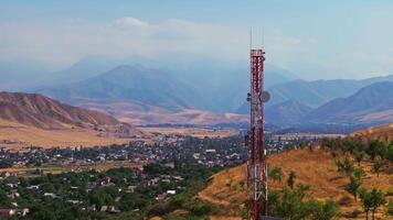 Drone footage showing a mountain village near with a telecom tower on a dry hill. The drone slowly passing by a tower with distant mountains in the background at late summer day. video